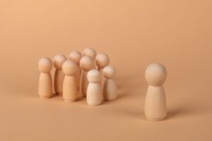 Symbolfoto: Holzfiguren auf einer Fläche, eine Figur steht der Gruppe gegenüber